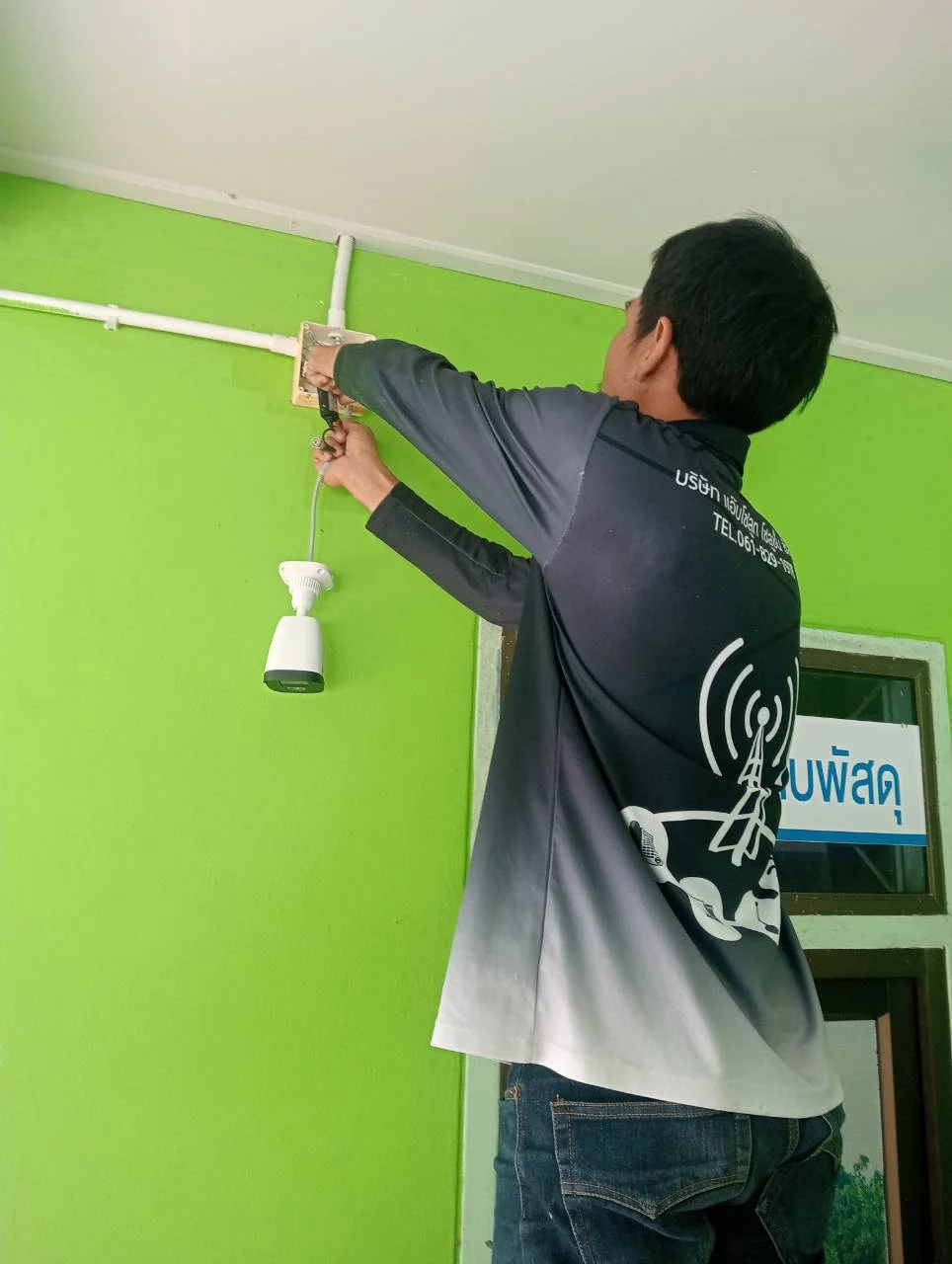 ช่างติดตั้งกล้องวงจรปิดและสายบริเวณผนังสีเขียว รพ.สต.บ้านบางคราม